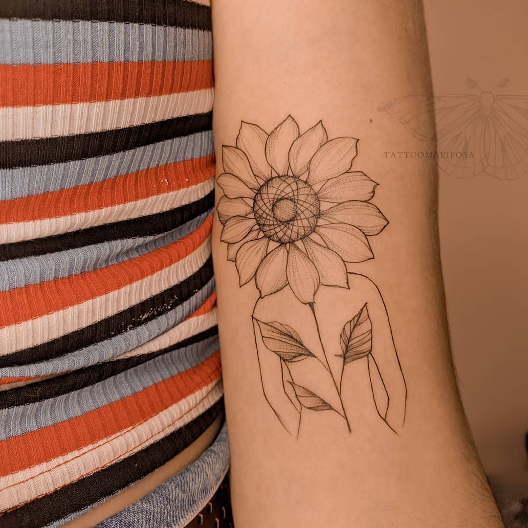 Tattoo of a figure with a sunflower head and butterfly wings on a forearm