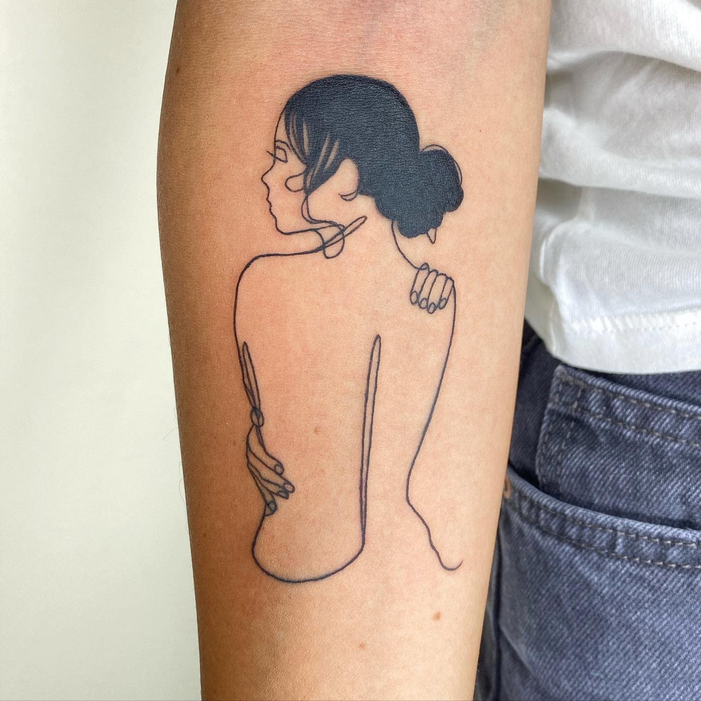 Minimalist tattoo of a woman with closed eyes and a bun, embracing herself