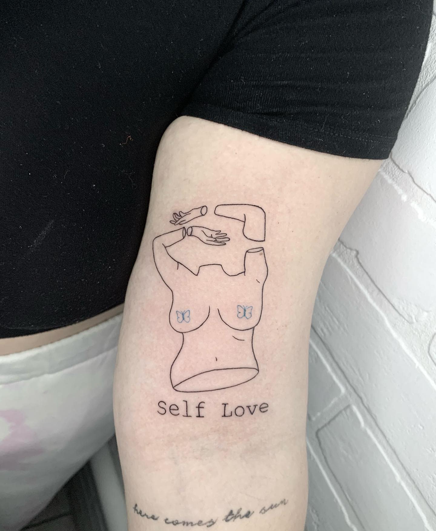 Line art tattoo on arm of a woman with "Self Love" text and two butterflies