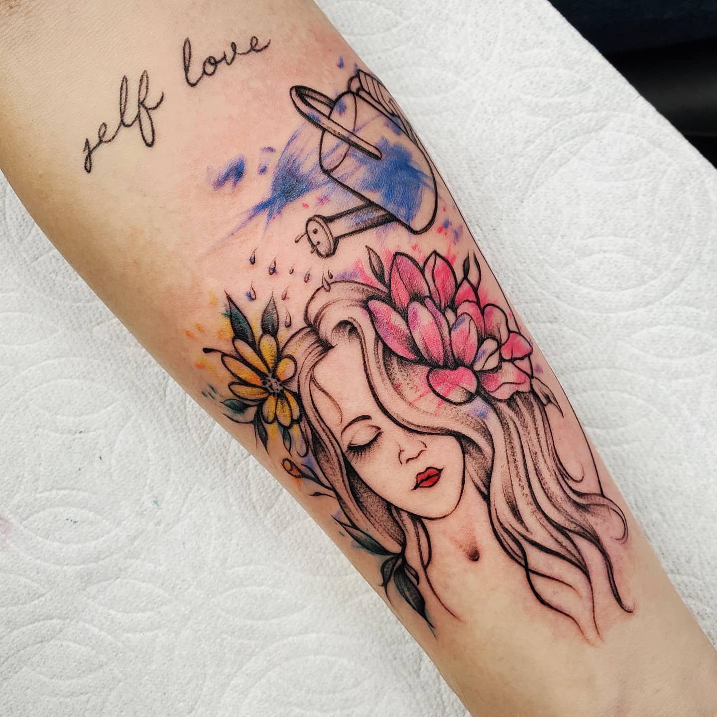 Tattoo of a woman's face with flowers and a watering can plus the text "self love"