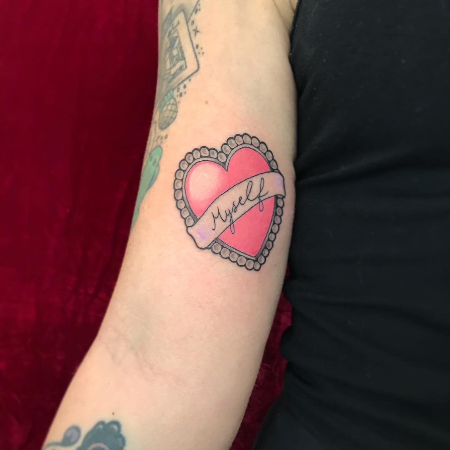 Tattoo of a heart with the word "Myself" inside a banner on an arm