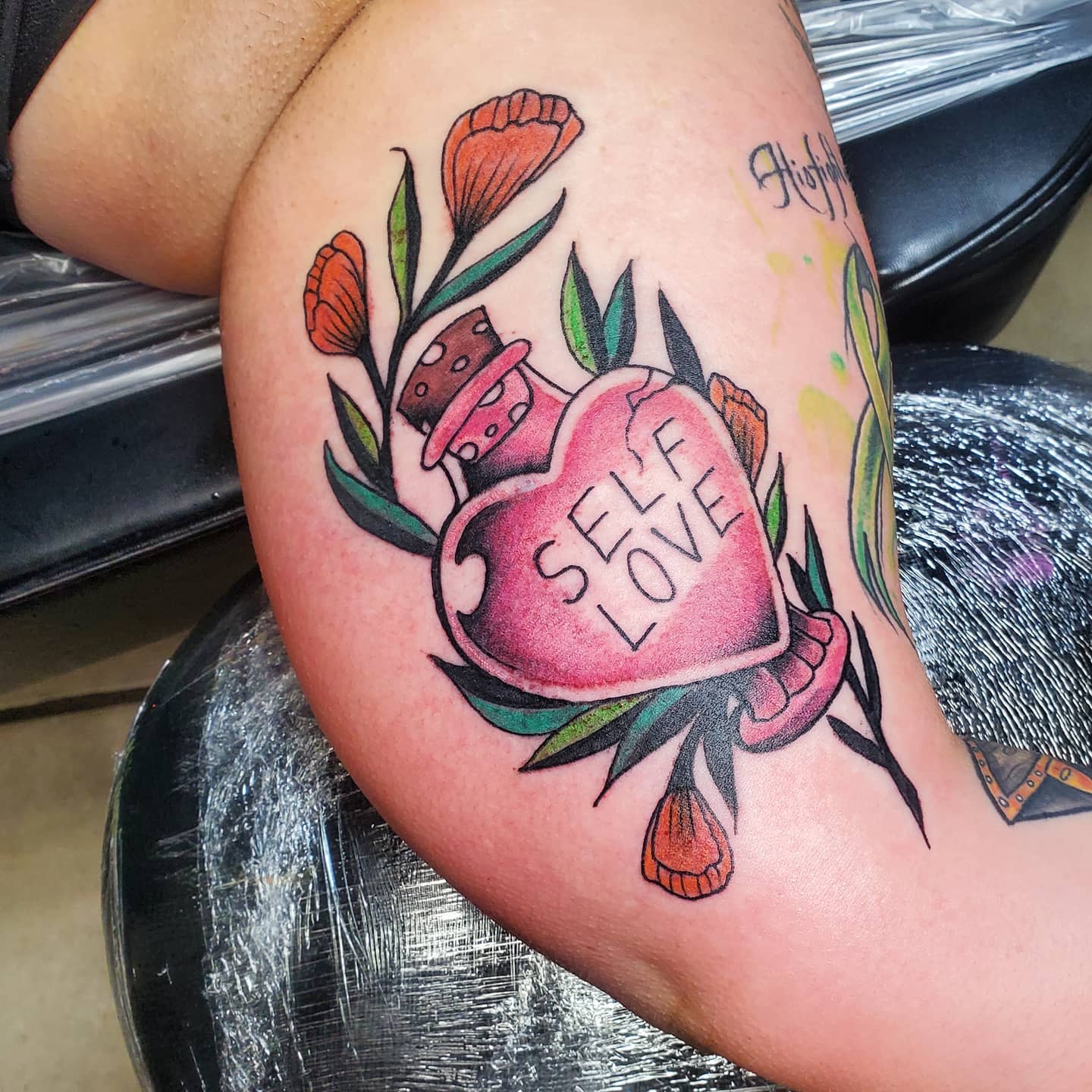 Tattoo of a heart with 'Self Love' and flowers on an arm