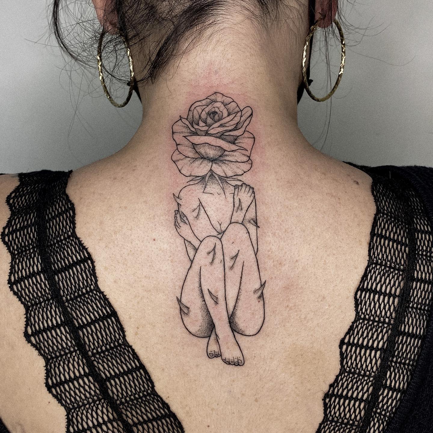 Tattoo of a figure with a rose as a head on the back of someone's neck