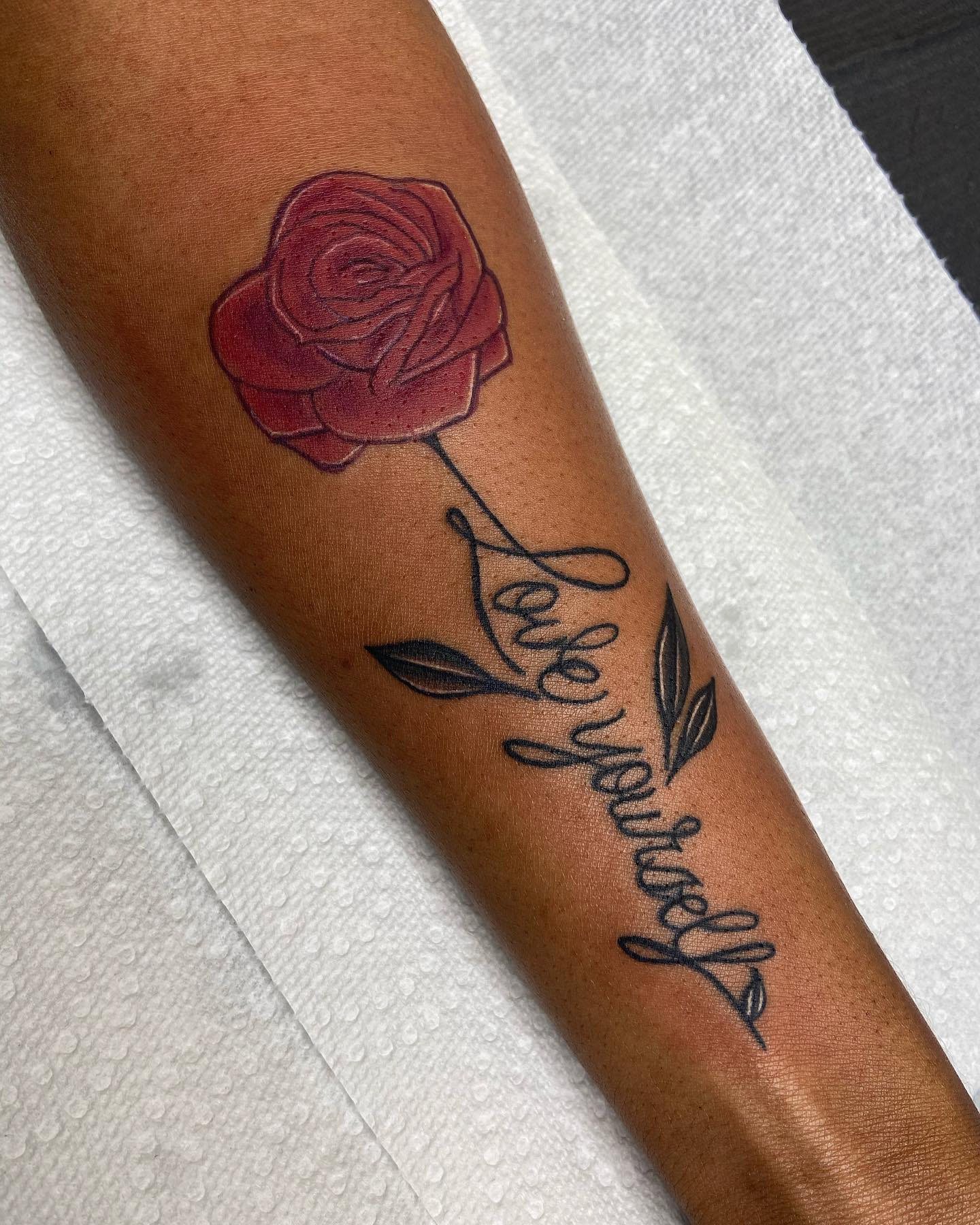 Tattoo of a red rose with "Love yourself" in cursive on an arm