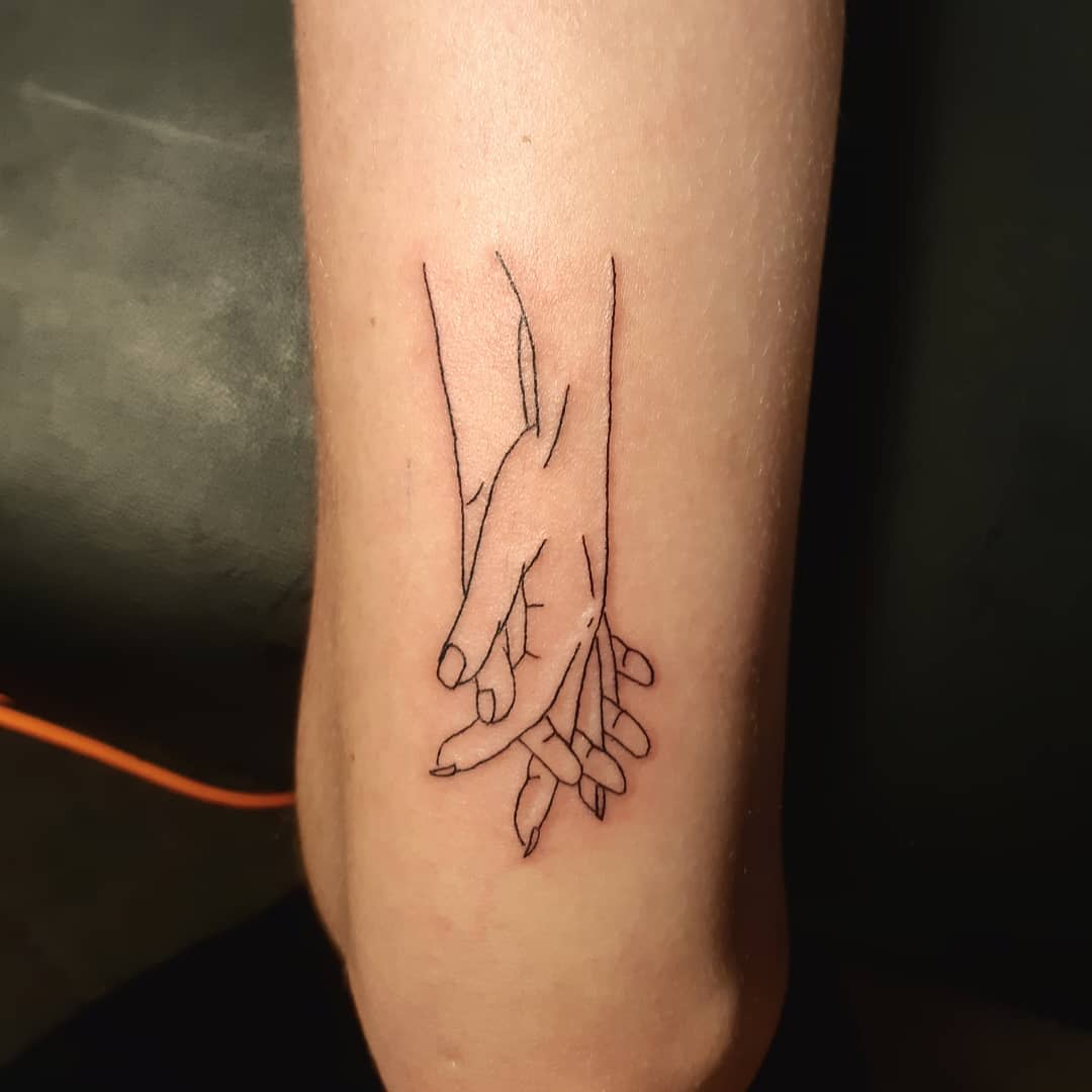Minimalist line tattoo of two hands intertwined on the inner forearm