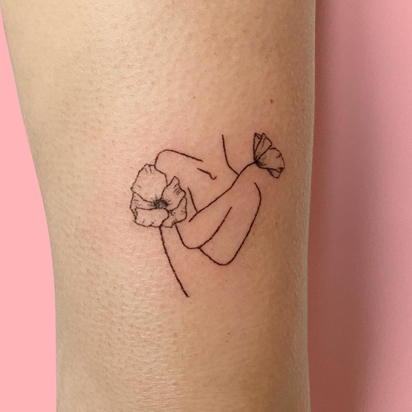 Minimalist tattoo of two hands intertwined, each holding a flower