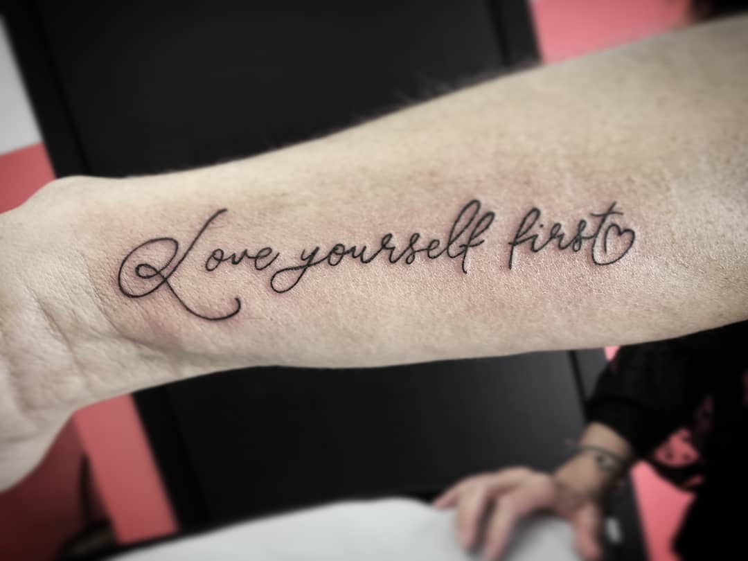 Love yourself first tattoo on the inner forearm in cursive script