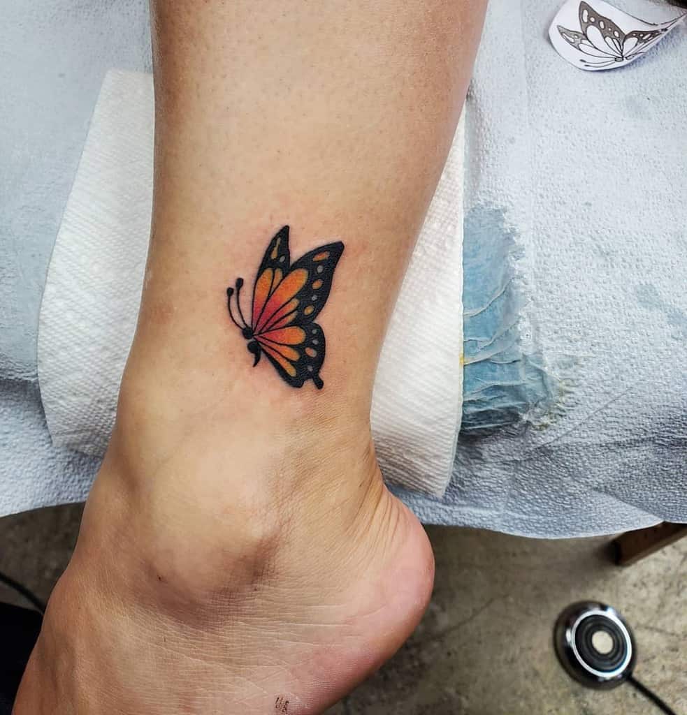 A vibrant orange and black butterfly tattoo on the ankle, symbolizing personal transformation and freedom, with clean, detailed lines