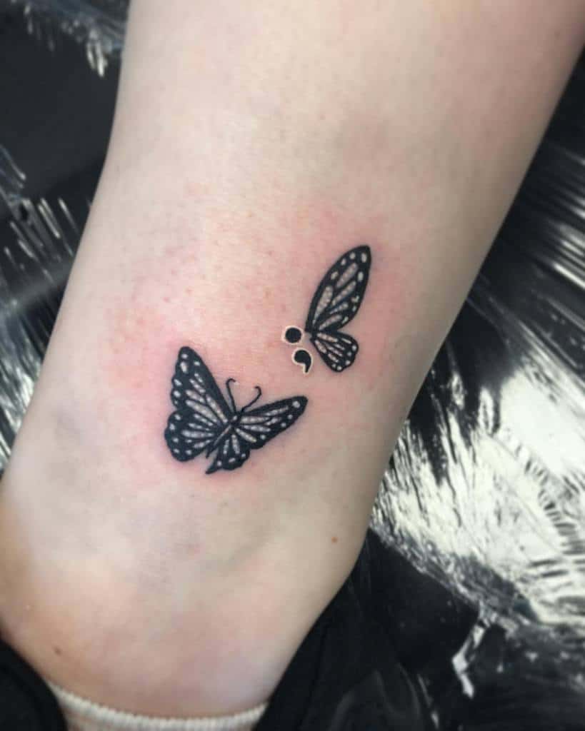 A black and white butterfly tattoo featuring a semicolon design on the ankle, symbolizing mental health awareness and survival