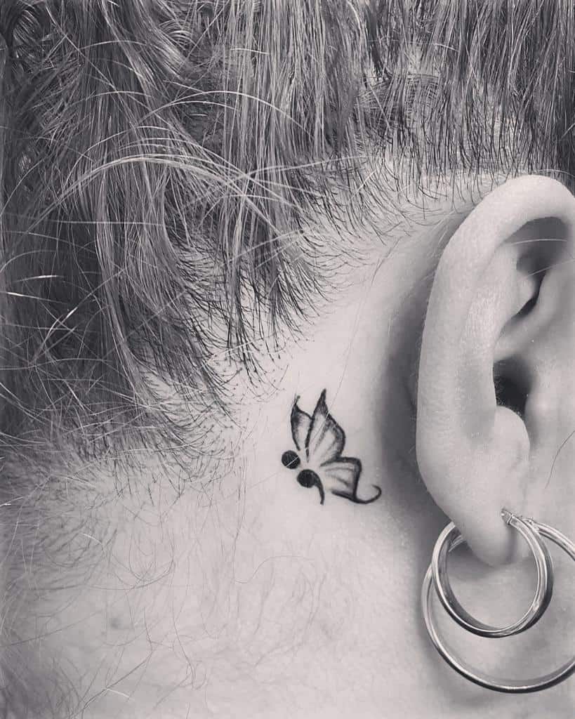 A small, elegant semicolon butterfly tattoo behind the ear, symbolizing resilience, mental health awareness, and the journey toward healing