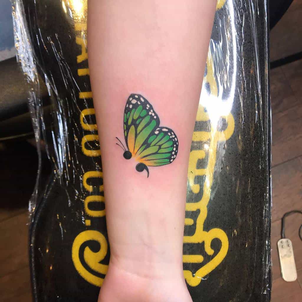 A vibrant green and yellow semicolon butterfly tattoo on the forearm, symbolizing transformation, hope, and mental health awareness, with a bold and colorful design