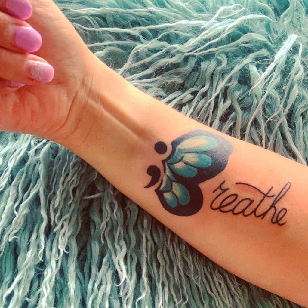 A bold blue semicolon butterfly tattoo on the forearm, paired with the word "Breathe," symbolizing calmness, resilience, and mental health awareness