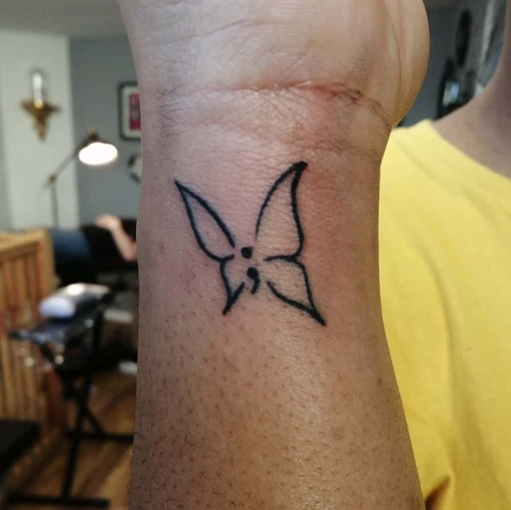 A minimalist semicolon butterfly outline tattoo on the wrist, symbolizing strength, resilience, and the continuation of one's journey with a simple yet powerful design