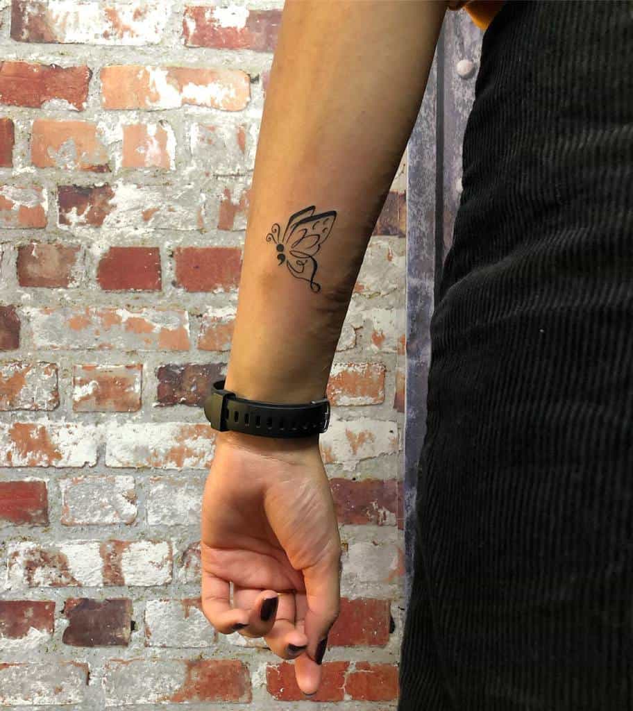 A minimalist semicolon butterfly tattoo on the forearm, featuring delicate lines and swirls, symbolizing personal growth, mental health awareness, and the beauty of resilience