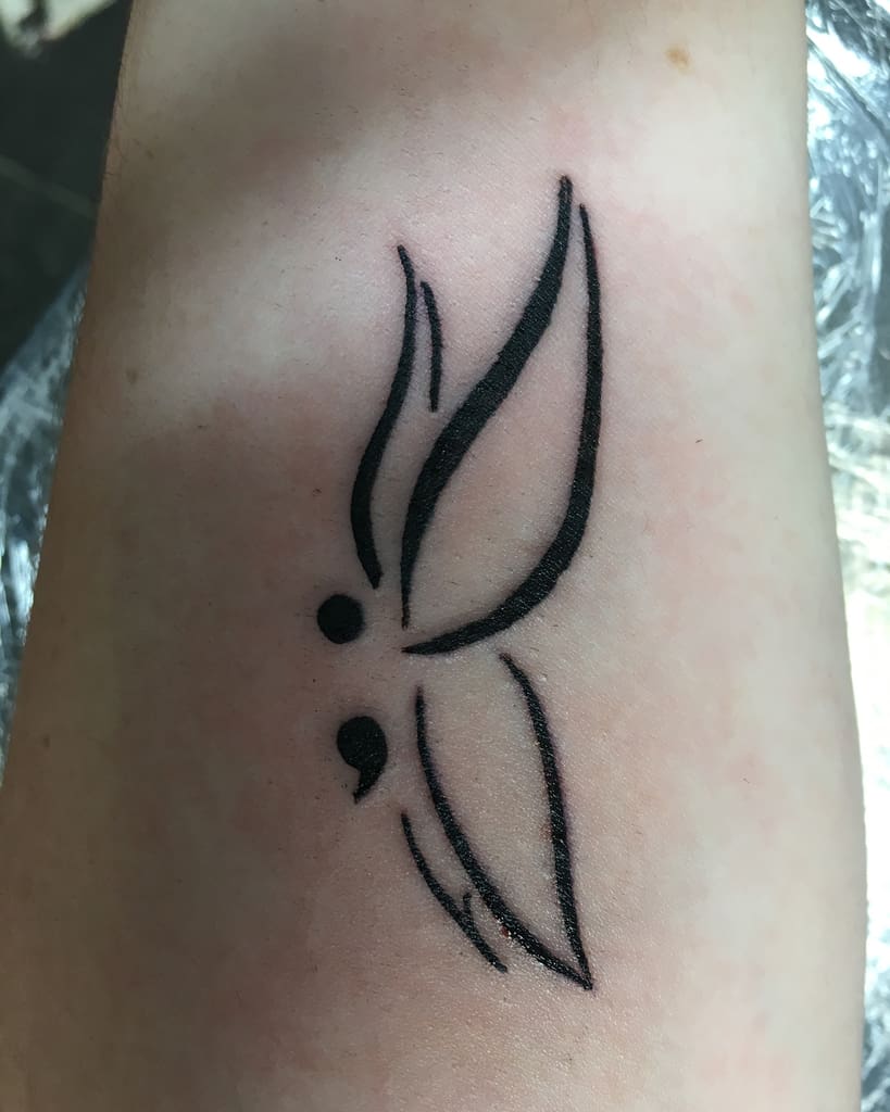 A minimalist semicolon butterfly tattoo with bold, clean lines, symbolizing strength, mental health awareness, and the journey of overcoming personal challenges with a simple yet striking design