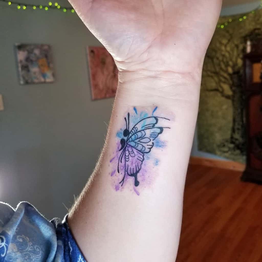 A colorful butterfly tattoo with semicolon on a person's inner wrist
