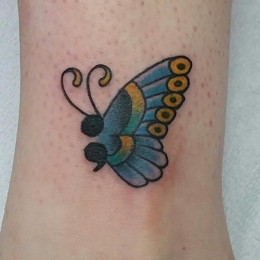 Colorful butterfly tattoo with blue, yellow, and green wings on light skin