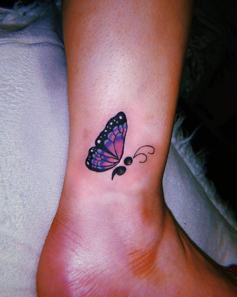 Delicate purple butterfly tattoo with a semicolon design on the ankle, symbolizing hope, resilience, and new beginnings.