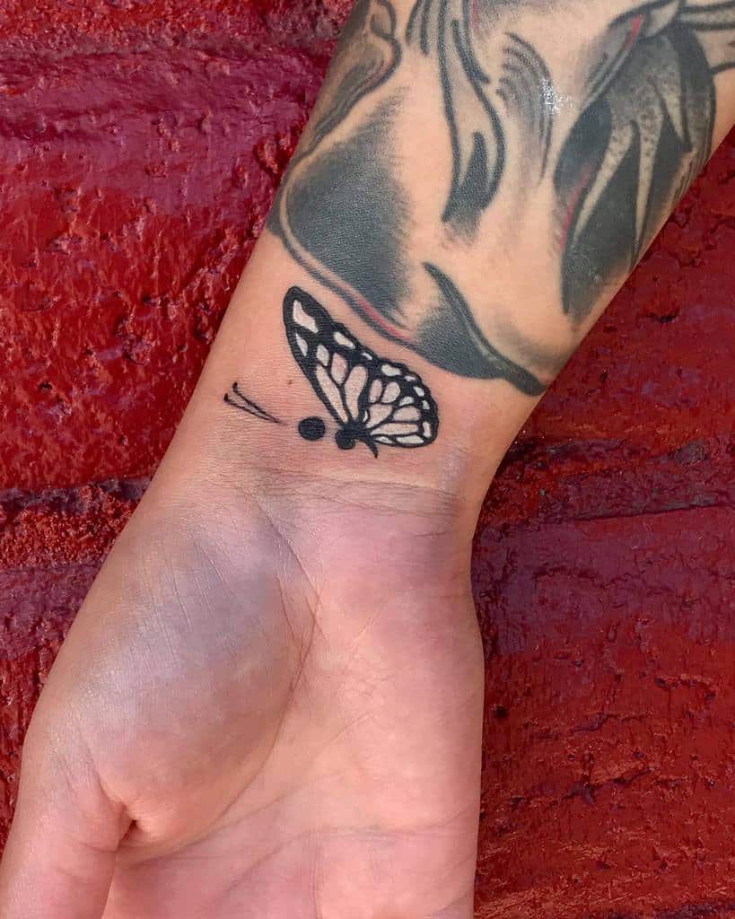 A simple black ink semicolon butterfly tattoo on the wrist, symbolizing strength, survival, and mental health awareness
