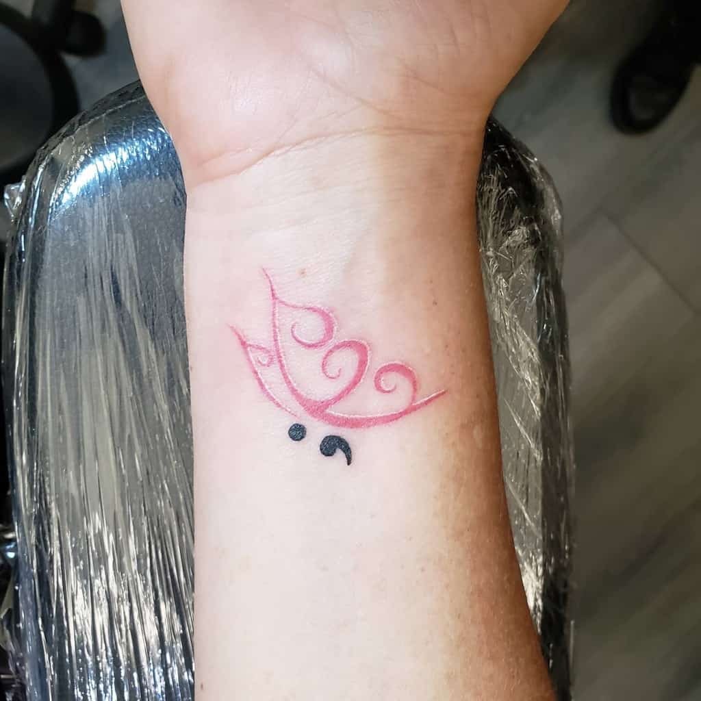 A minimalist pink butterfly tattoo with a semicolon body on the wrist, symbolizing mental health awareness and survival
