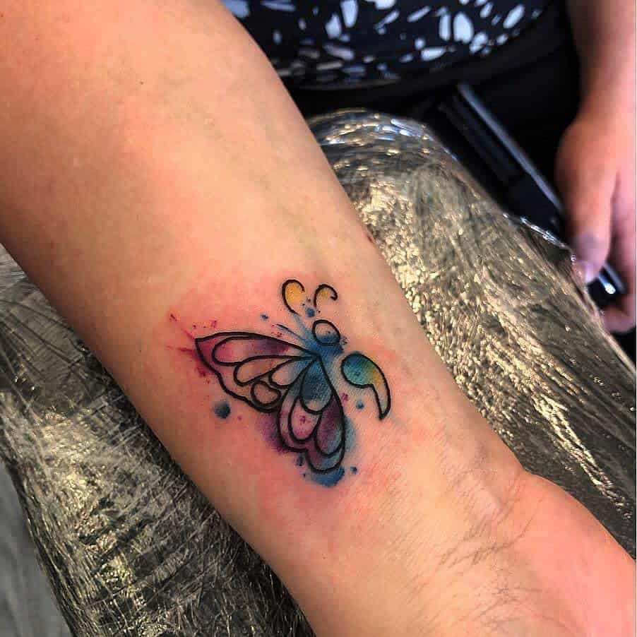 A vibrant watercolor butterfly tattoo with a semicolon body on the wrist, symbolizing mental health awareness and personal growth