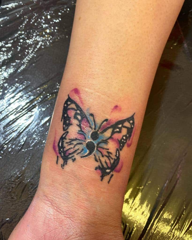 A black and colorful watercolor butterfly tattoo with a semicolon body on the wrist, symbolizing resilience, hope, and mental health awareness