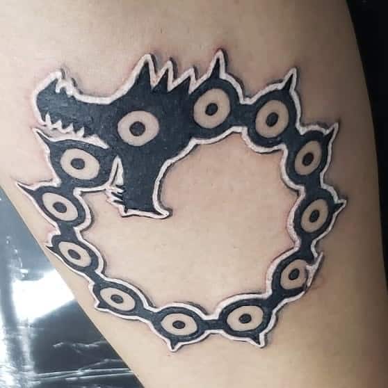Black and white tattoo of the symbol representing the Dragon's Sin of Wrath from The Seven Deadly Sins, featuring a dragon's head within a circle of eyes