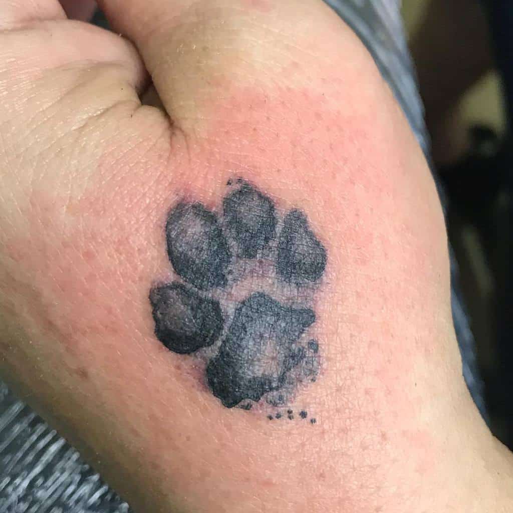 A black cat paw print tattoo graces the back of a person's hand
