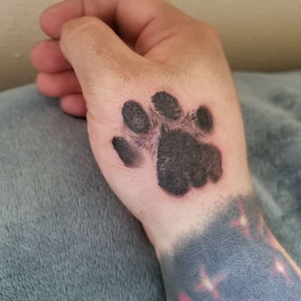 Tattoo of a shaded black cat paw print on the back of a person's hand