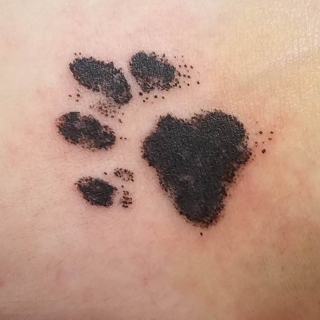 A shaded black cat paw print tattoo on light skin