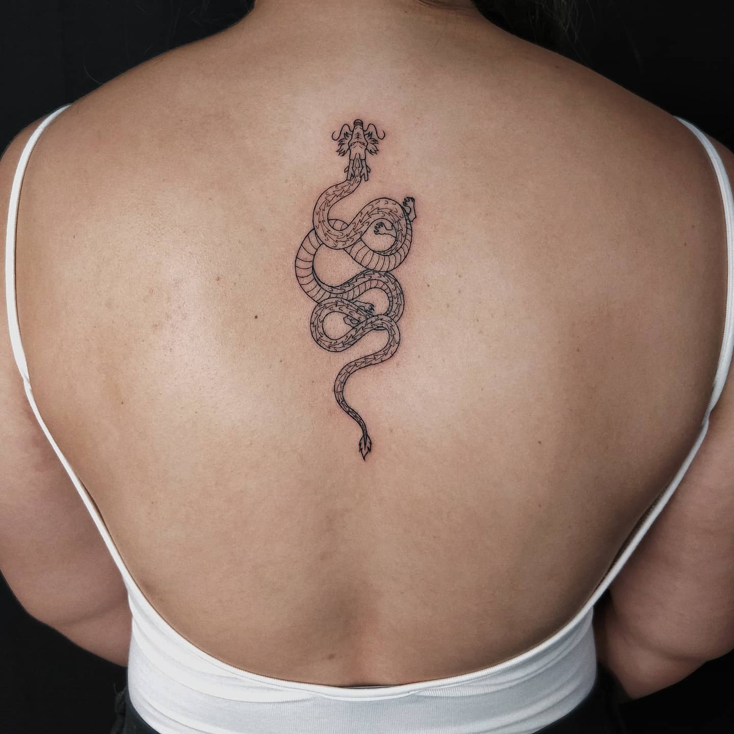 A simple, fine-lined Shenron tattoo on the upper back, depicting the dragon's elegance