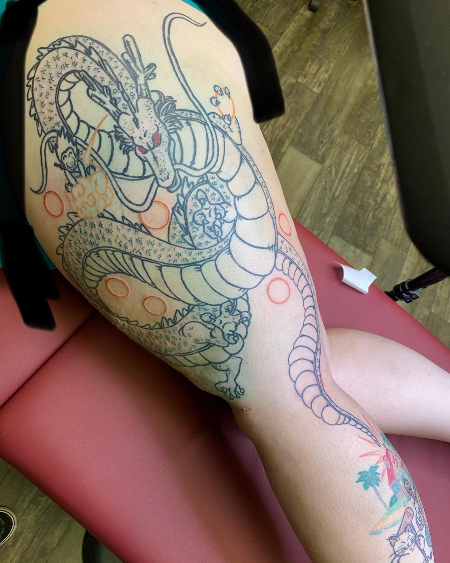 Large outline tattoo of Shenron on the thigh, featuring Goku and Dragon Balls in progress