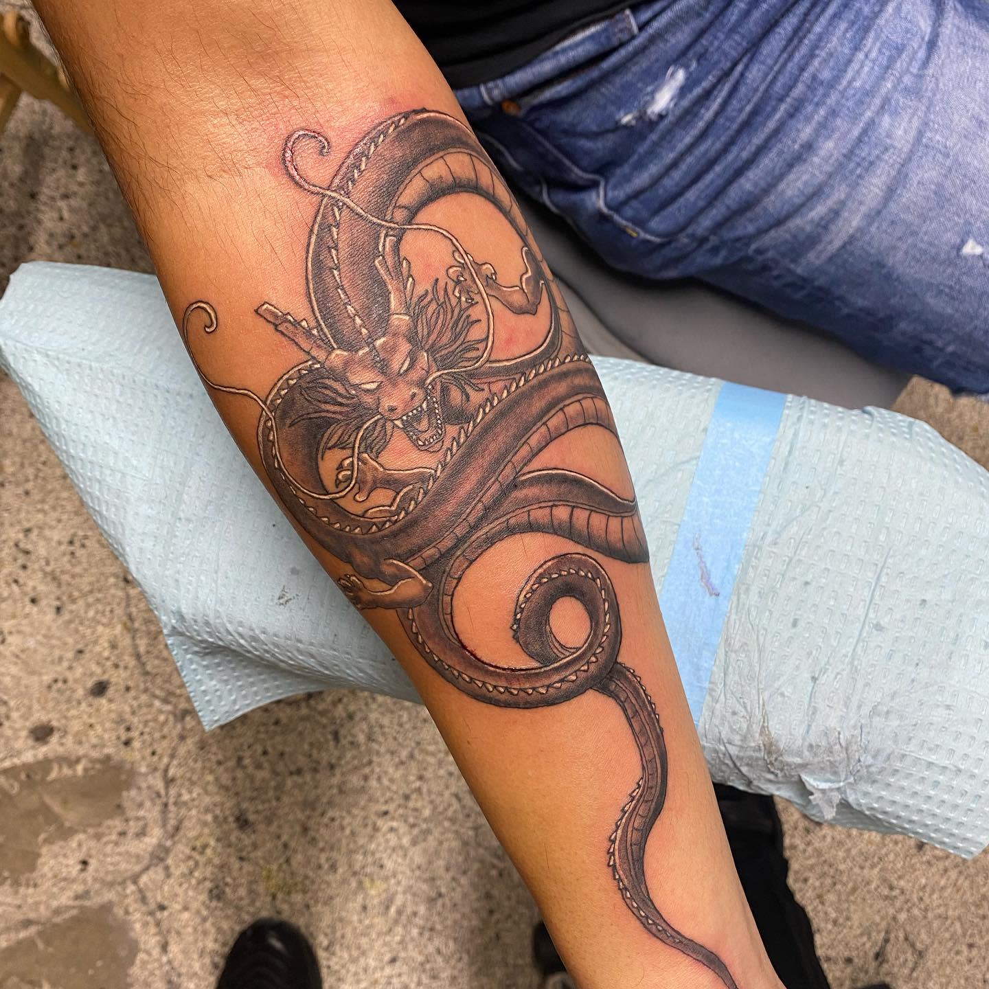Detailed black and grey tattoo of Shenron wrapped around the forearm, showcasing intricate shading