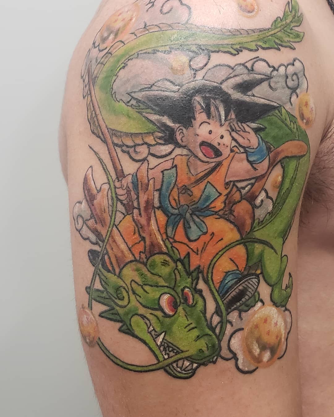 Tattoo of Goku riding Shenron on an upper arm with dragon balls surrounding them