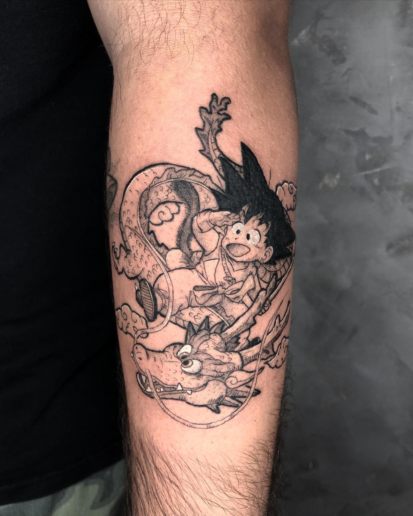 Black and grey forearm tattoo of Goku riding Shenron, capturing a playful and adventurous scene