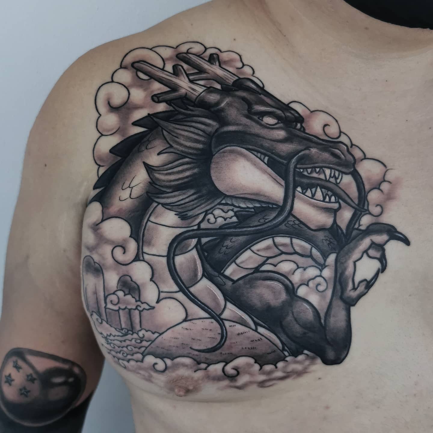Detailed black and grey tattoo of Shenron on the chest, with dramatic shading and cloud effects