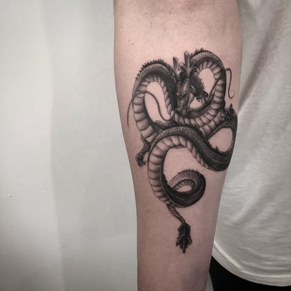 Detailed black and grey tattoo of Shenron on the forearm, featuring smooth shading and intricate line work