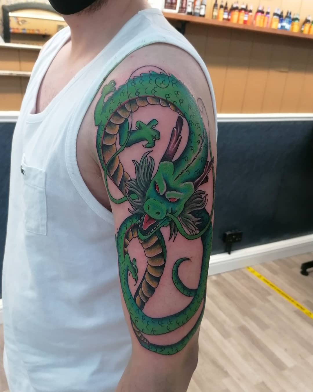Bold and colorful tattoo of Shenron wrapping around the upper arm, with vivid green scales and dynamic shading