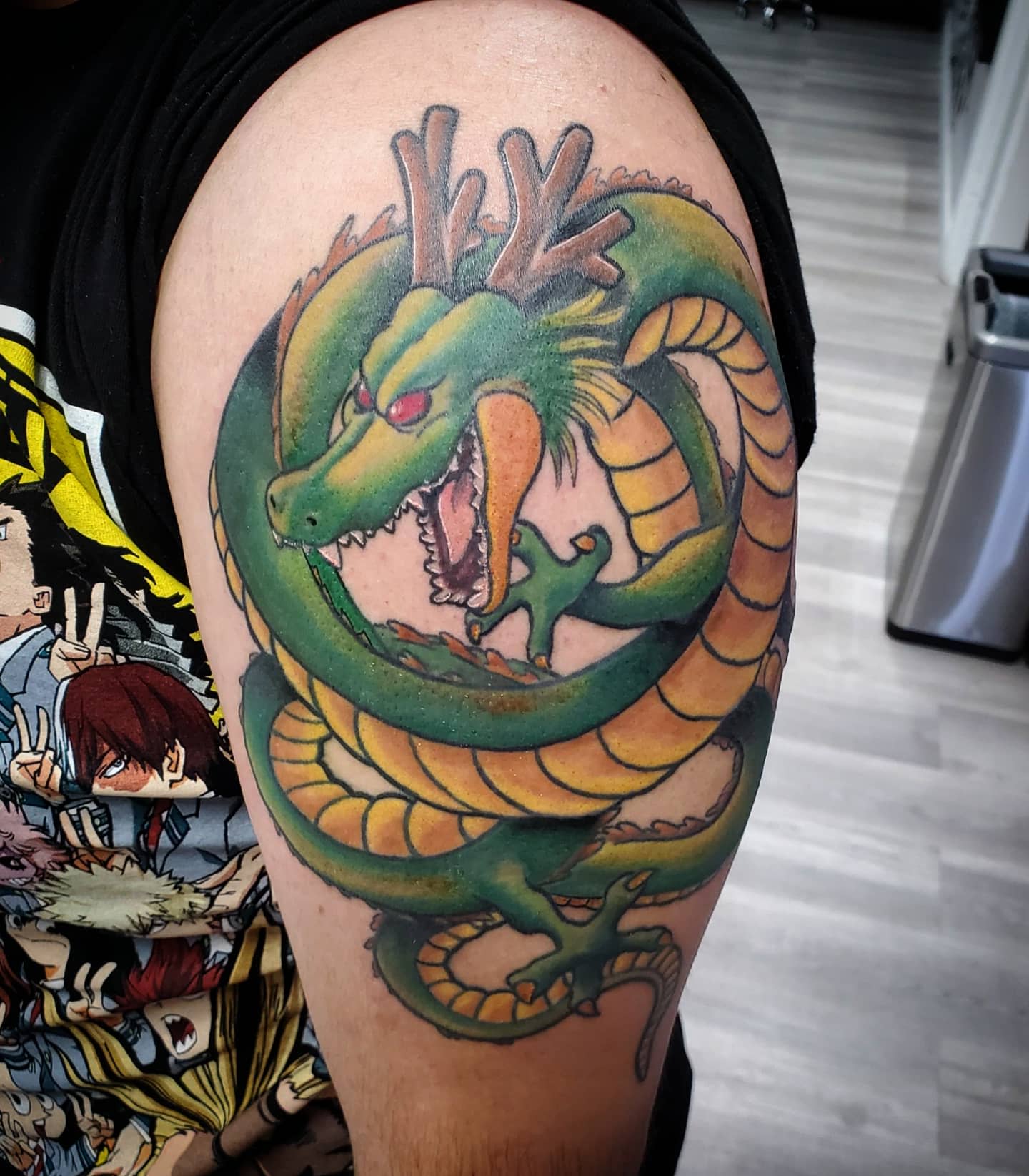 A striking tattoo of Shenron on the upper arm, featuring vibrant green and yellow tones with fierce expression