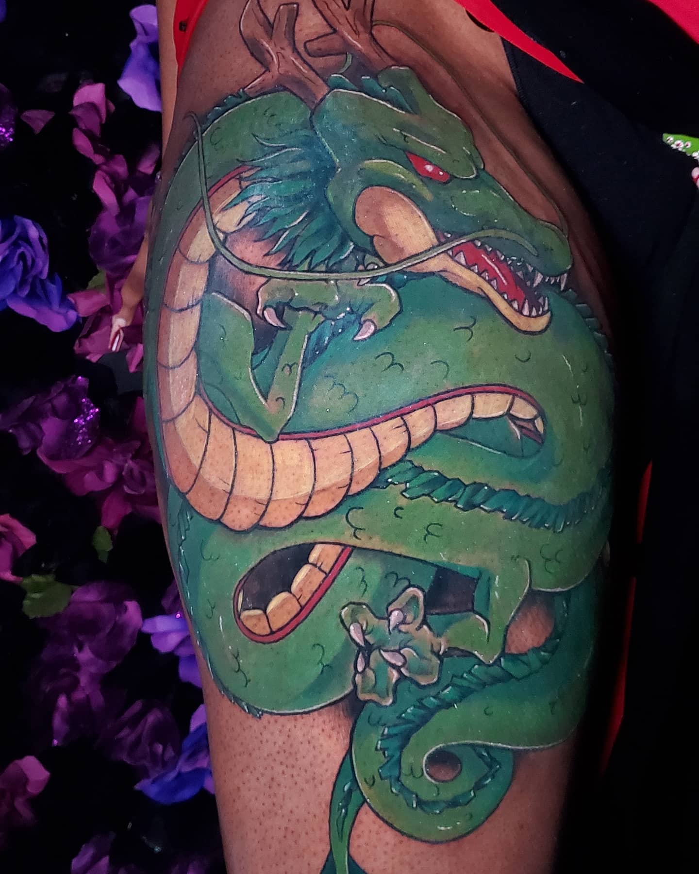 A striking and colorful tattoo of Shenron on the thigh, with vivid green tones and sharp detailing