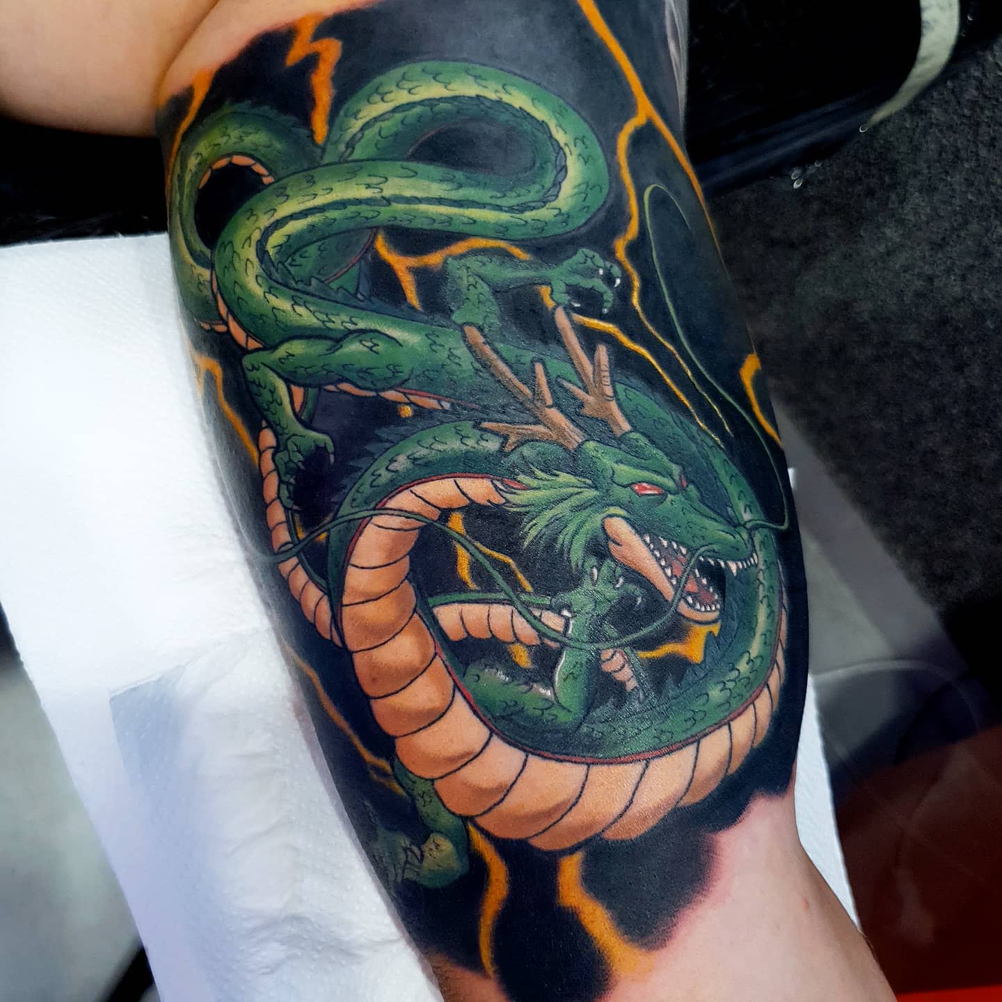 Bold and dynamic Shenron tattoo on the arm, with detailed shading and striking orange lightning effects