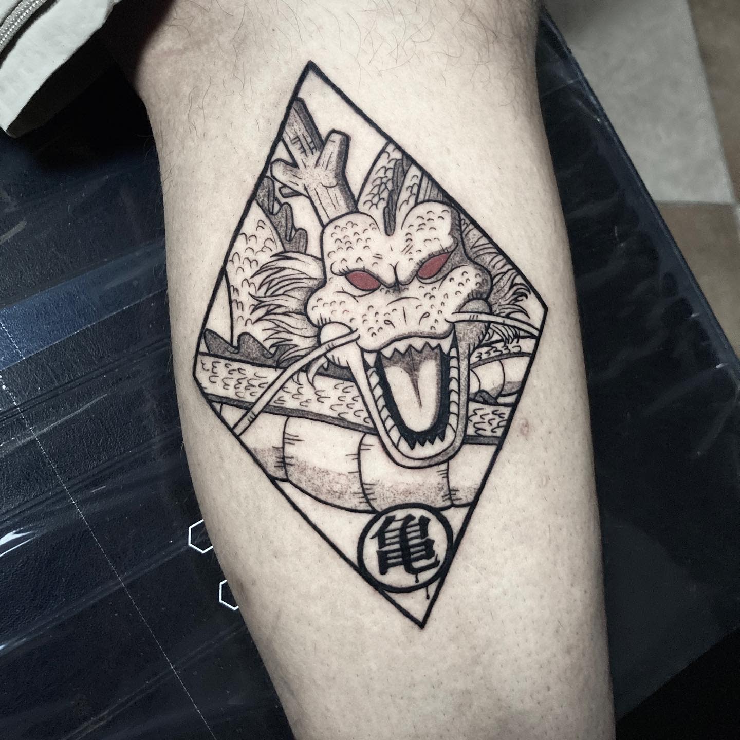 Black and grey tattoo of Shenron enclosed in a diamond-shaped frame, highlighting his fierce expression and intricate details