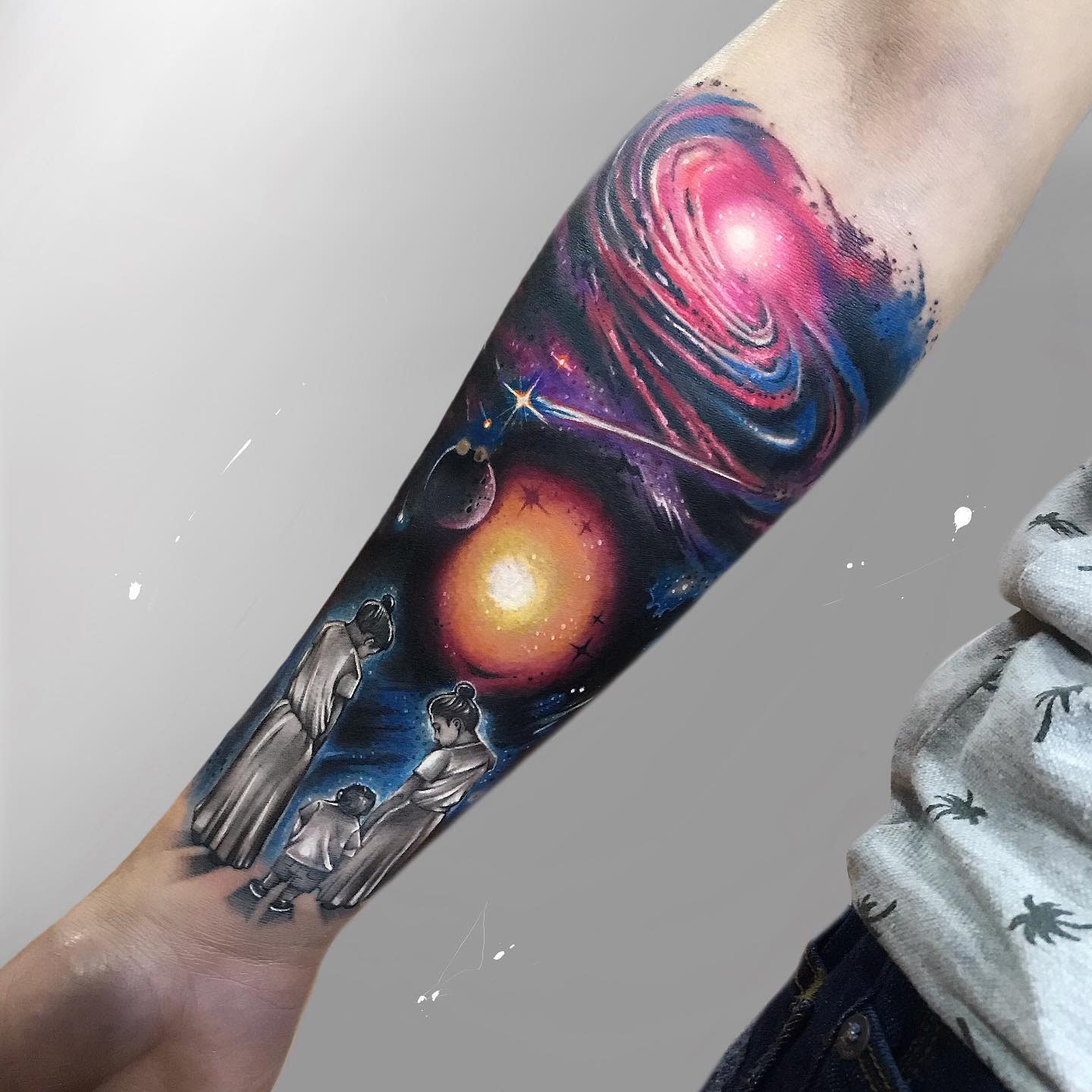 Forearm tattoo featuring a family looking at a galaxy scene