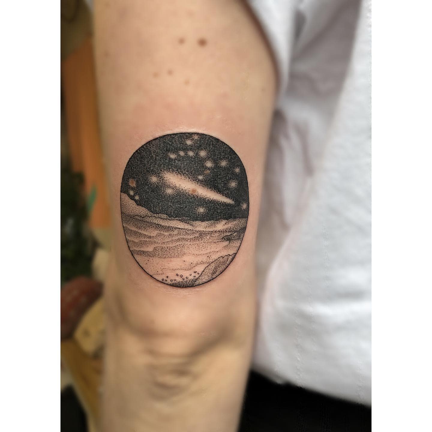 A tattoo of a night sky and shooting star on the back of an upper arm
