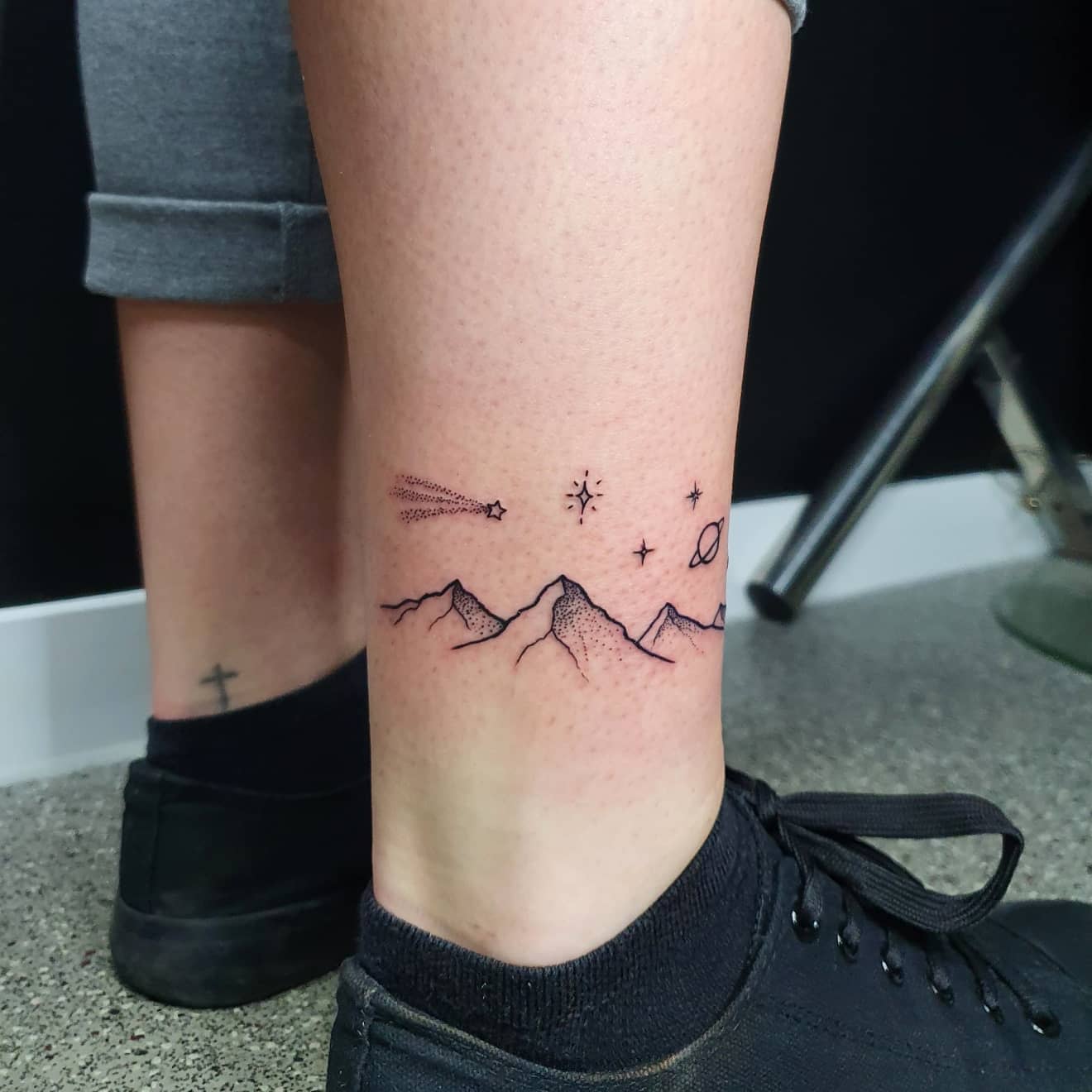 Tattoo of mountains and outer space elements on an ankle