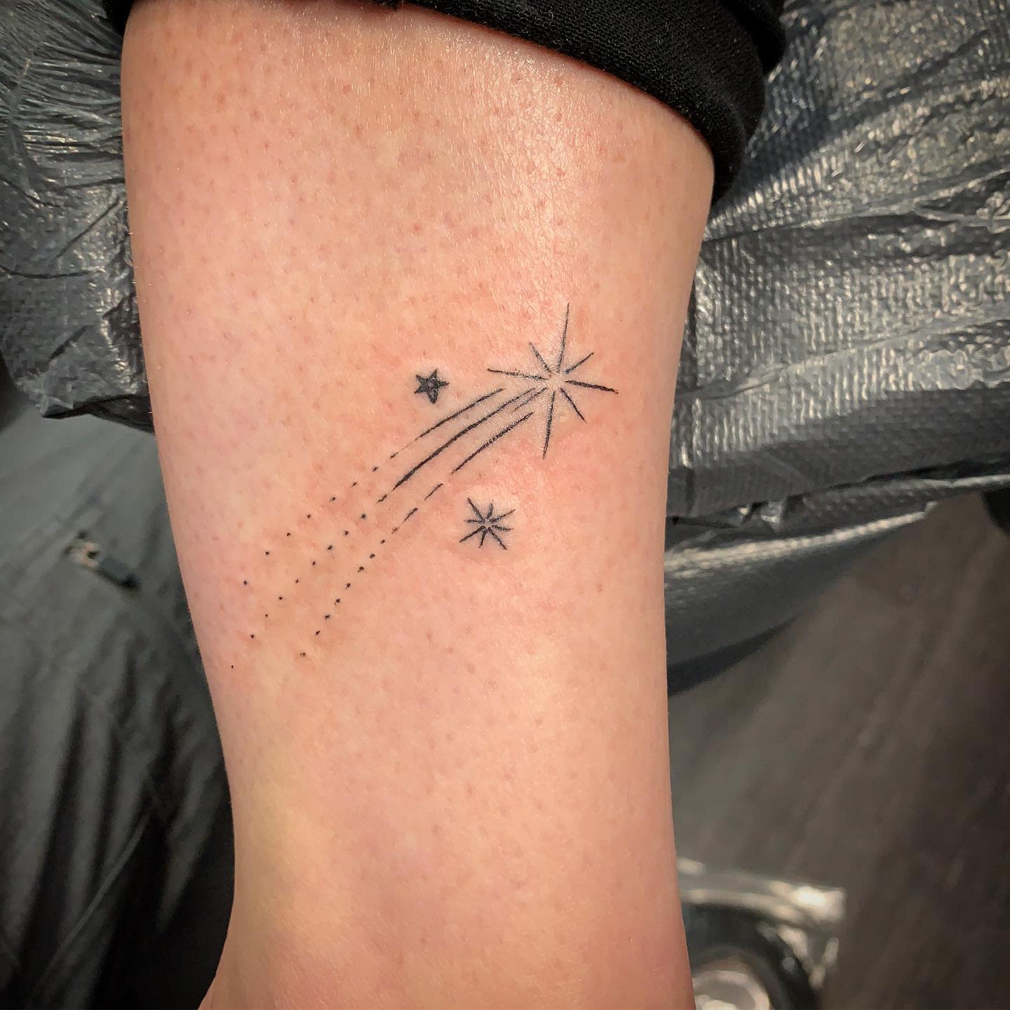 Tattoo on forearm featuring a shooting star with two smaller stars in a minimalistic style