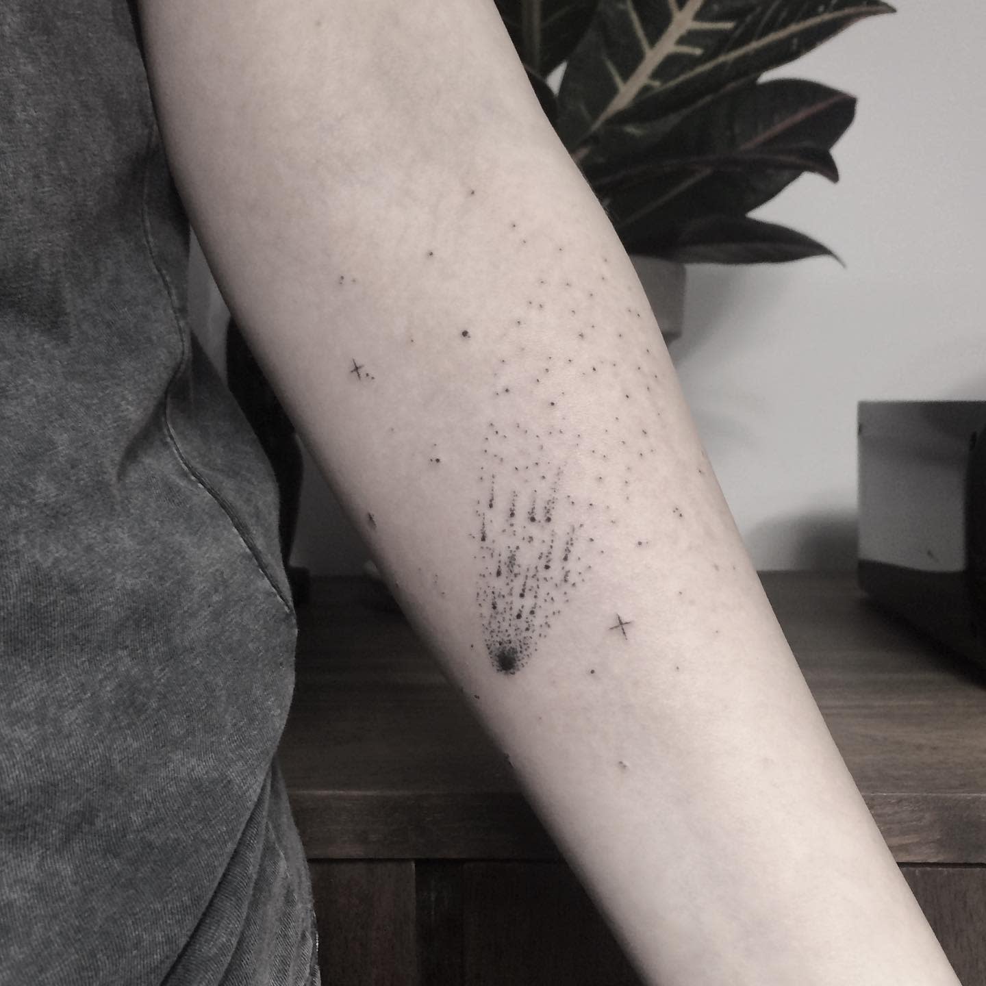 Forearm tattoo featuring black dot-work resembling a starry sky with a shooting star