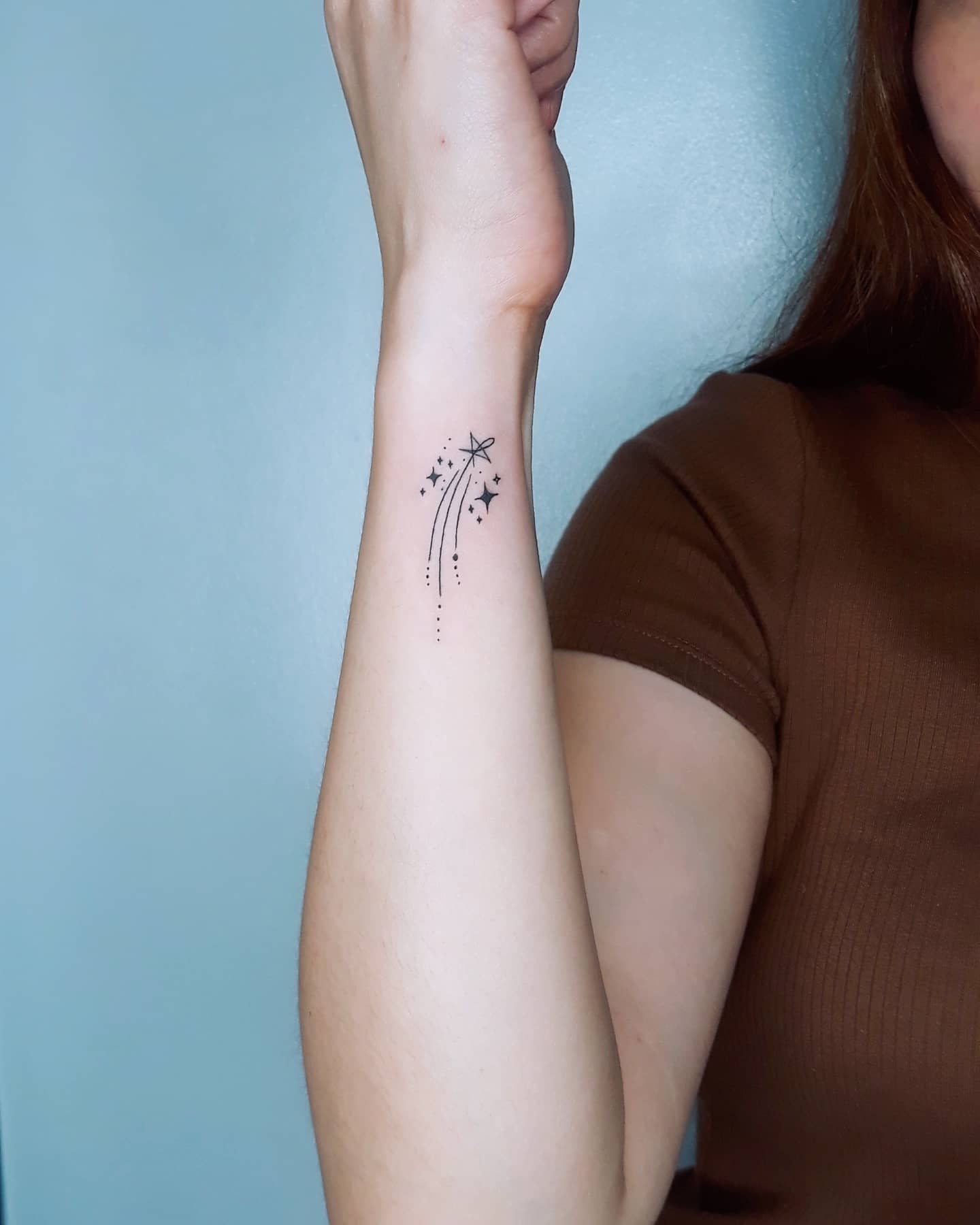 Forearm tattoo of a shooting star with a trail of small stars and dots