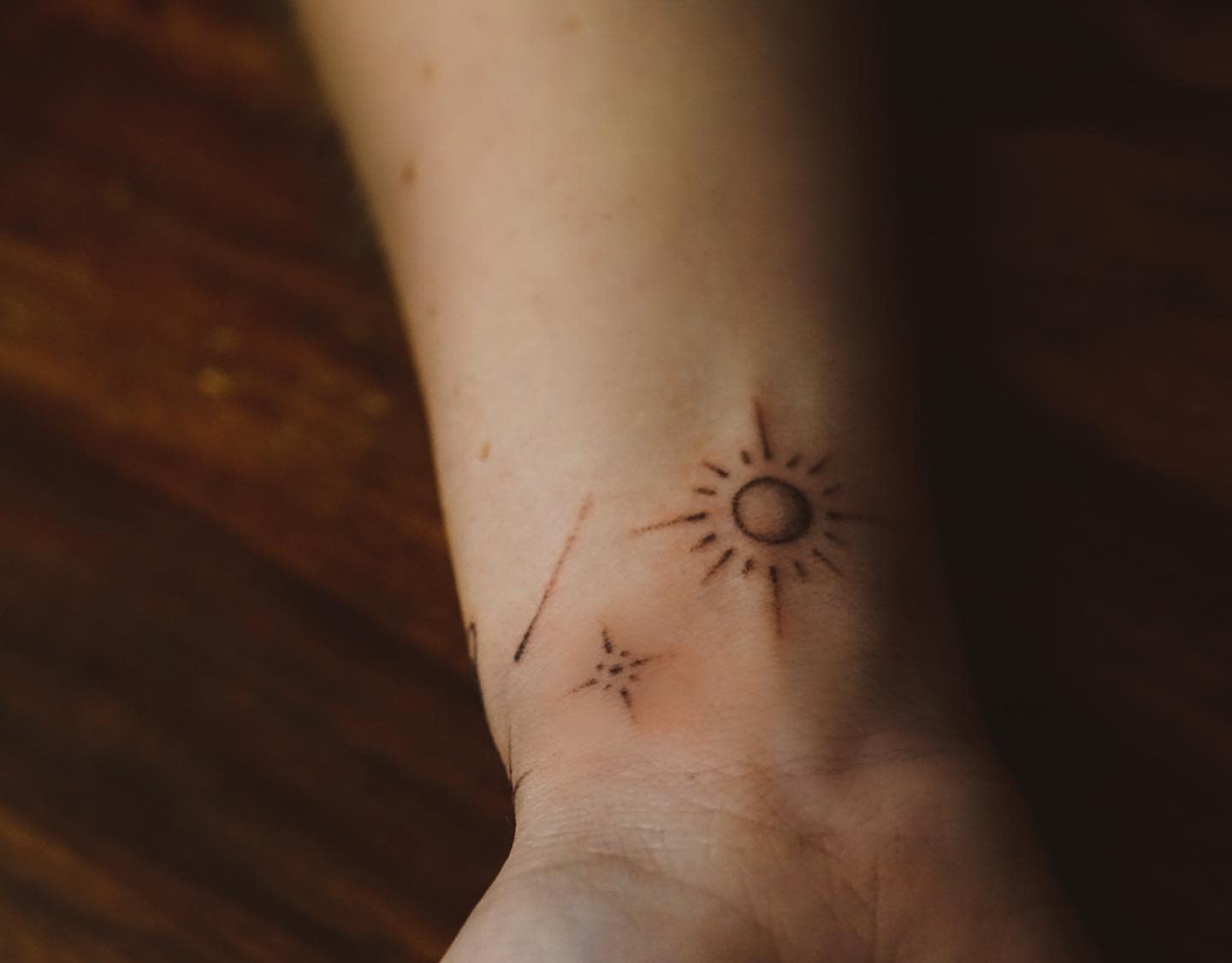 Minimalist wrist tattoo featuring a sun, star, and lines