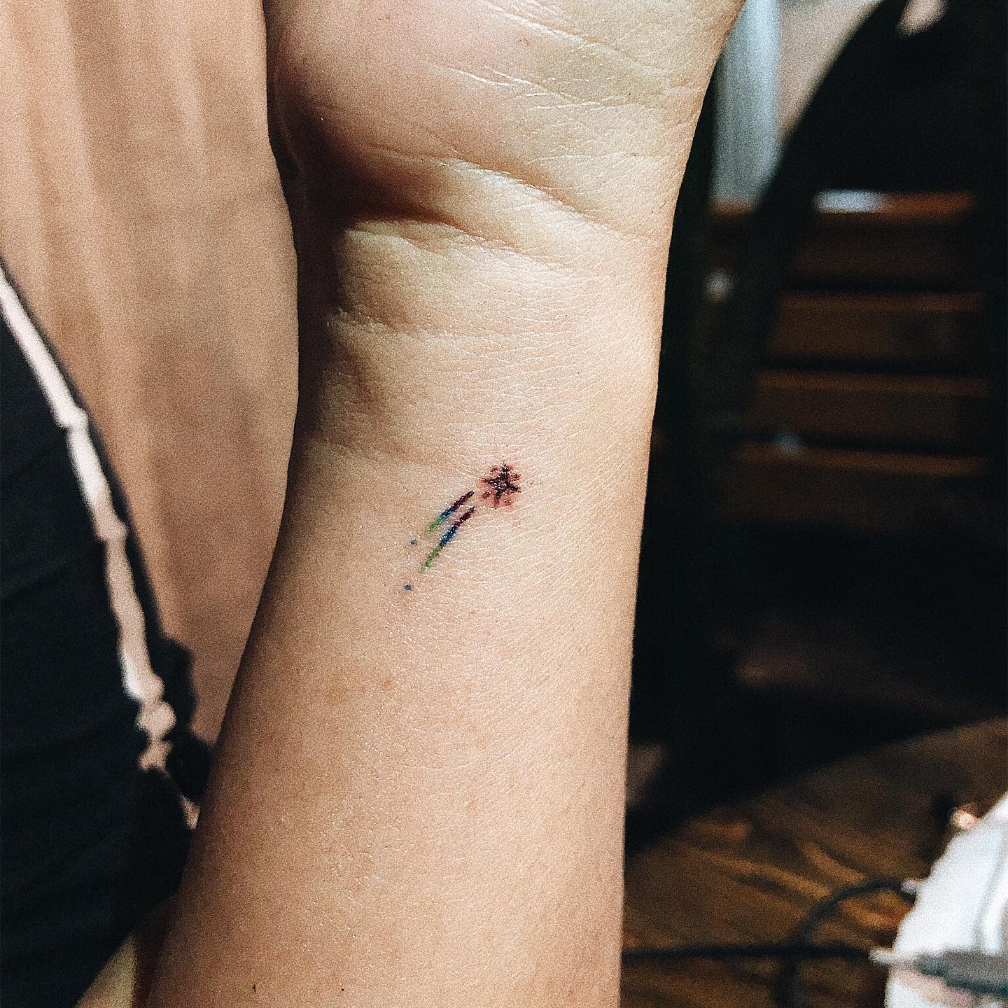 Small, colorful star tattoo with three lines trailing on a wrist